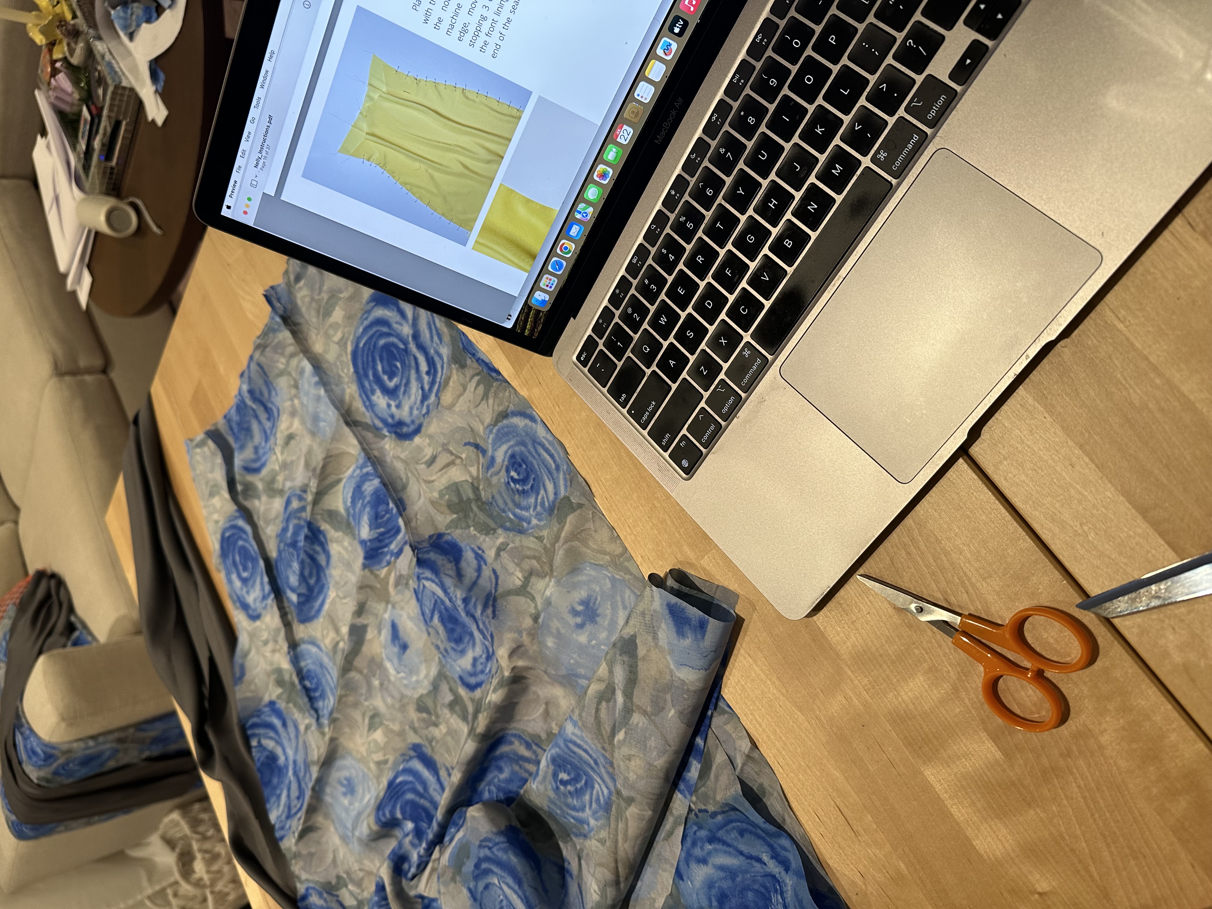 Laptop open to the Nelly Dress pattern instructions next to the cut rose print silk